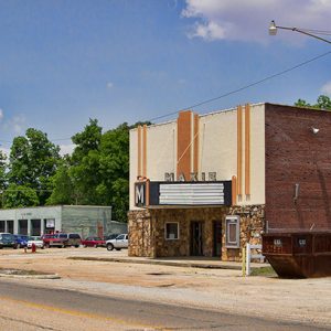 Brick and stone "Makie theater" building on multilane street with brick buildings and garage building in the background