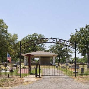 Cemetery with iron gate and building and flag on gravel road