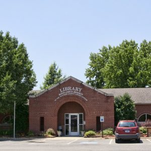 Single-story brick library building and parking lot with one parked car