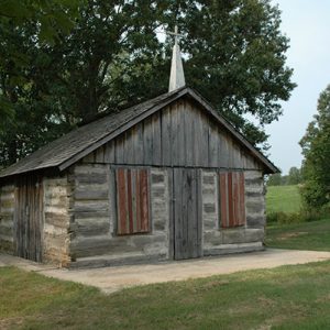 small log cabin church with steeple and cross on grass with trees