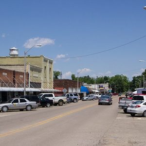 Street with brick storefronts parked cars and water tower in the background