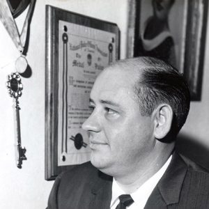 White man in suit and tie looking at award plaques on wall