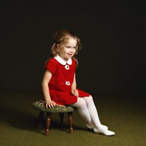 Young white girl in red dress sitting on a stool smiling