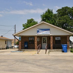 Small brick building and parking lot with satellite dish and blue recycling can