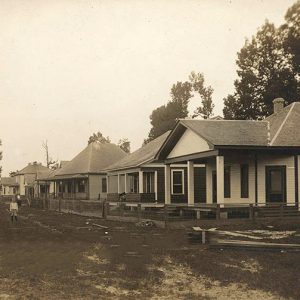 Child standing on street in front of single-story houses with covered porches