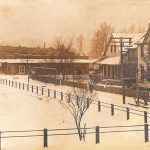 Multistory town buildings on snow covered streets with fenced-in park in the foreground