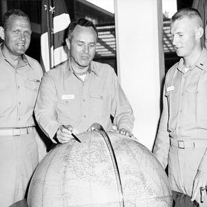 Three white men in military uniform examingin globe with American flag in the background