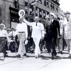 White men in suits and hats leading a parade down city street