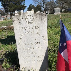 Weathered white gravestone in cemetery with small flag