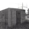 Small concrete building with iron door and water tower in the background