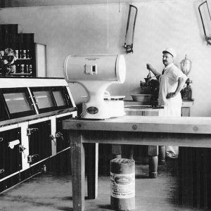 White man in apron standing among meat cutting implements