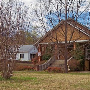 Brick church building with trees and sign with house behind it