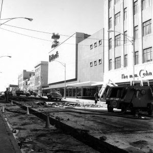 Machinery and workers digging up city street across from multistory Dillards and M. M. Cohn department stores