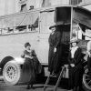 White man and three white women in hats and dresses posing with bus