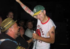 White man in hat with tattoos on stage with white crowd