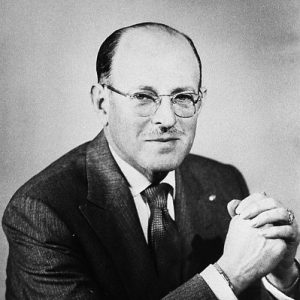 white man in glasses posed with hands folded in front