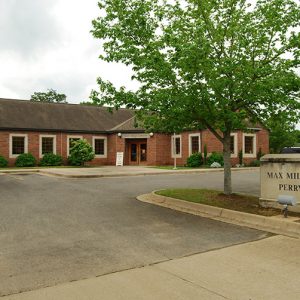 Single-story brick building on parking lot with tree and sign