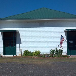 Single-story brick building painted white with green roof and sign in front saying "museum open Saturday"