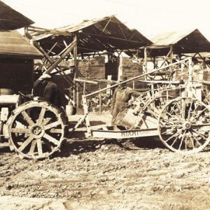 White men in suits and farmer in a hat with tractor and trailer