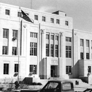 Multistory stone art deco building with smooth walls relief columns dentil entablature steps flagpole and mailbox