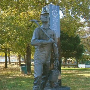 Statue of man with mining equipment on base and polished stone column behind it