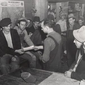 White man handing other white man piece of paper among group of others