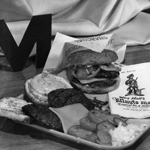 Hamburger and toppings displayed on a food tray with "Wes Hall's Minute Man" napkins and letter "M"