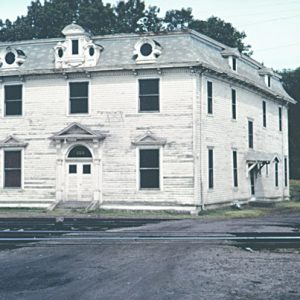 weathered two story wooden building at the intersection of train tracks and dirt road