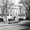 Multistory brick building with half sized upper story first floor window awnings and bare trees and cars parked in front