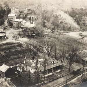 Aerial view of mining buildings and multistory house with covered porch outbuildings and garden