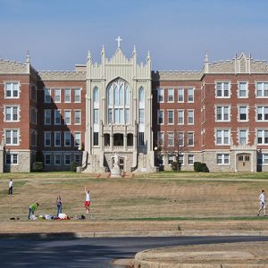 Four-story brick building with statue and arched windows and cross on top