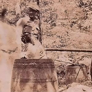 White man standing with whiskey still and barrels