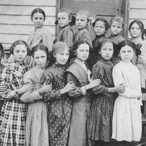 Group of white girls in dresses standing together outside building with wood siding