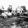 Crowded dirt road with storefront buildings horses and covered wagons