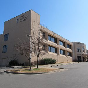 multistory school building with cross logo on its side and empty parking lot