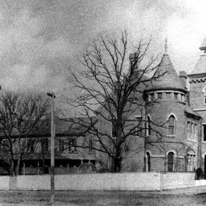 Two-story convent building with towers and wall on street corner with bare trees