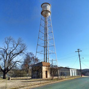 Looking up at water tower inside fence with outbuildings below it