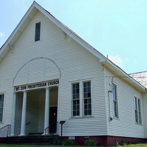 Single-story building with white wood siding and steeple roof and columned entry way