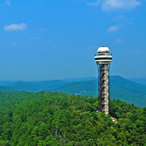 Observation tower on mountain top with tree covered mountains in the distance and blue skies