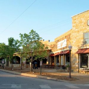 Town street with brick and stone storefronts and lighting fixtures, trees