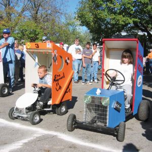 White children on go-carts modified to look like "outhouses" sitting at the starting line with crowd behind them