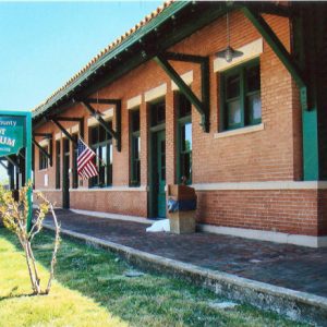 Close-up of single-story brick building with sidewalk and hanging sign on grass