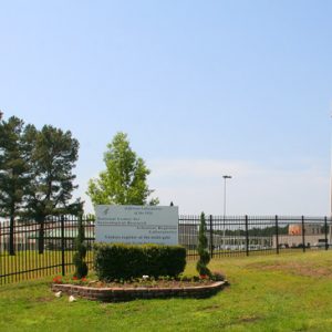 sign outside fence with three water towers and buildings in background