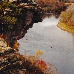 Rock outcropping above river with mountain in the background covered in autumn trees