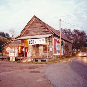 Single-story storefront with open gable roof and covered porch and prominent Pepsi signs on rural road