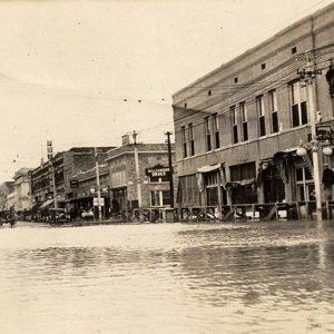 White men walking on elevated wooden walkway above flooded town streets