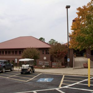 Brick building with red roof and tower and parking lot with cars and a golf card