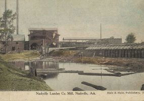 Multistory mill buildings with smoke stacks and logs floating on water in the foreground