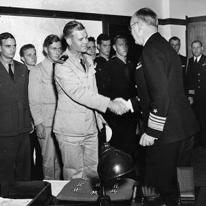 Young white men in military uniform with one of them shaking hands with older white officer