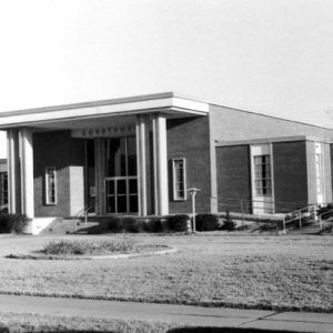 Brick building with rectangular columns vertical window sections steps wheelchair ramp and front lawn